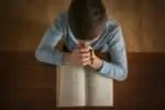Little boy with cross praying over Bible at table