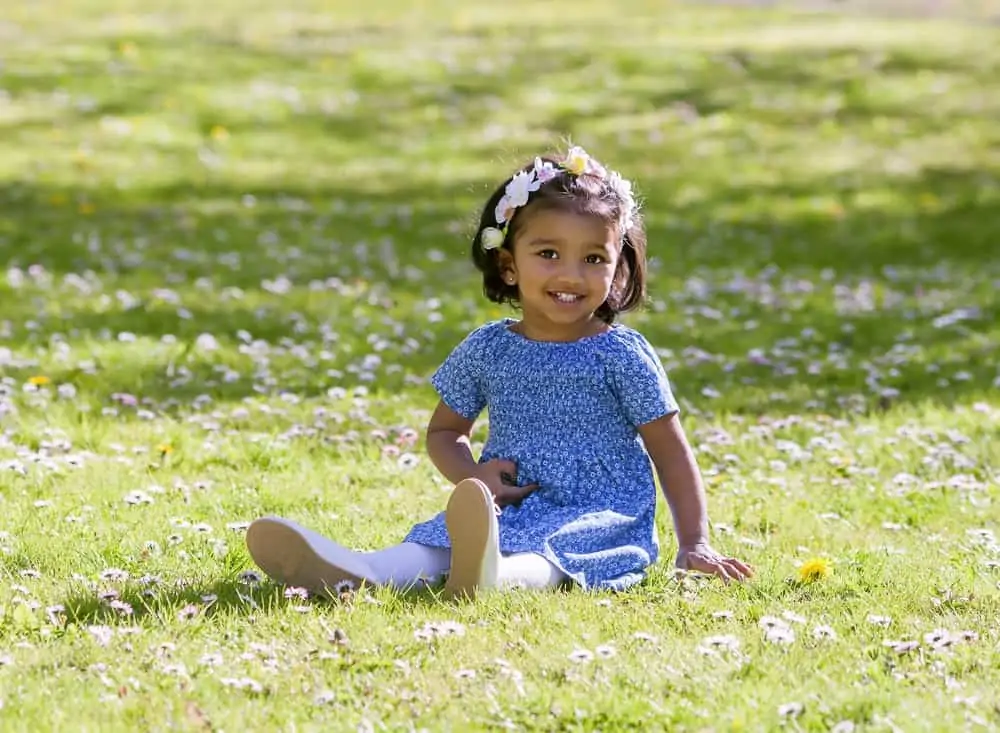 Hawaiian baby girl sitting on green meadow in sunny spring day