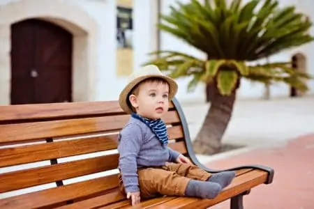 Baby boy wearing old-fashioned clothes and straw hat sitting on a bench