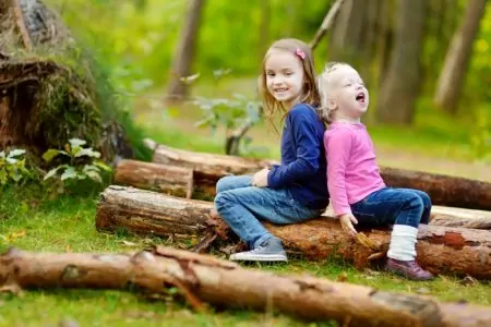 Two British sisters sitting on a big log in a forest