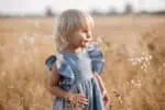 Adorable little blonde girl wearing blue dress in a field on a sunny day