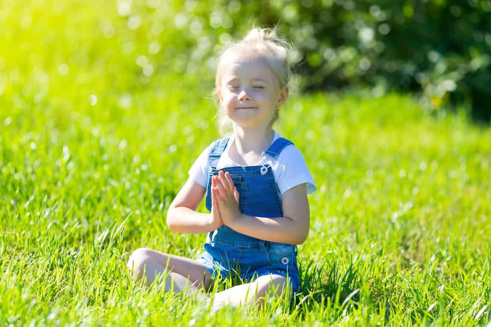 Slavic little girl sitting on the grass in a yoga pose