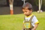 Adorable cute hindi little boy looking down while walking in garden