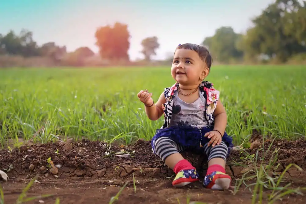 Hindi little girl sitting on soil in the farm