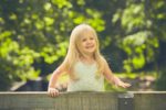 Scottish little girl wearing white dress standing on bench in the park smiling brightly on sunny day