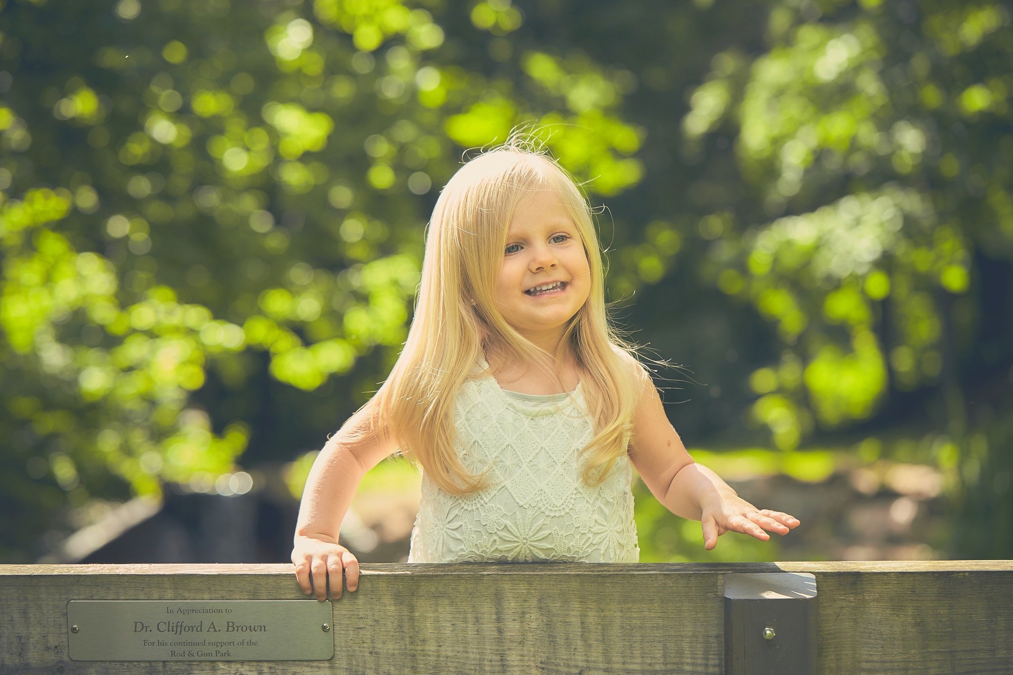 Scottish little girl wearing white dress standing on bench in the park smiling brightly on sunny day
