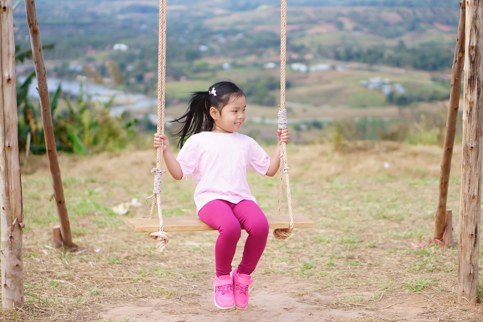 Thai adorable little girl on wooden swing smiling brightly