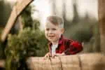 Danish smiling young boy leaning on wooden fence outdoors