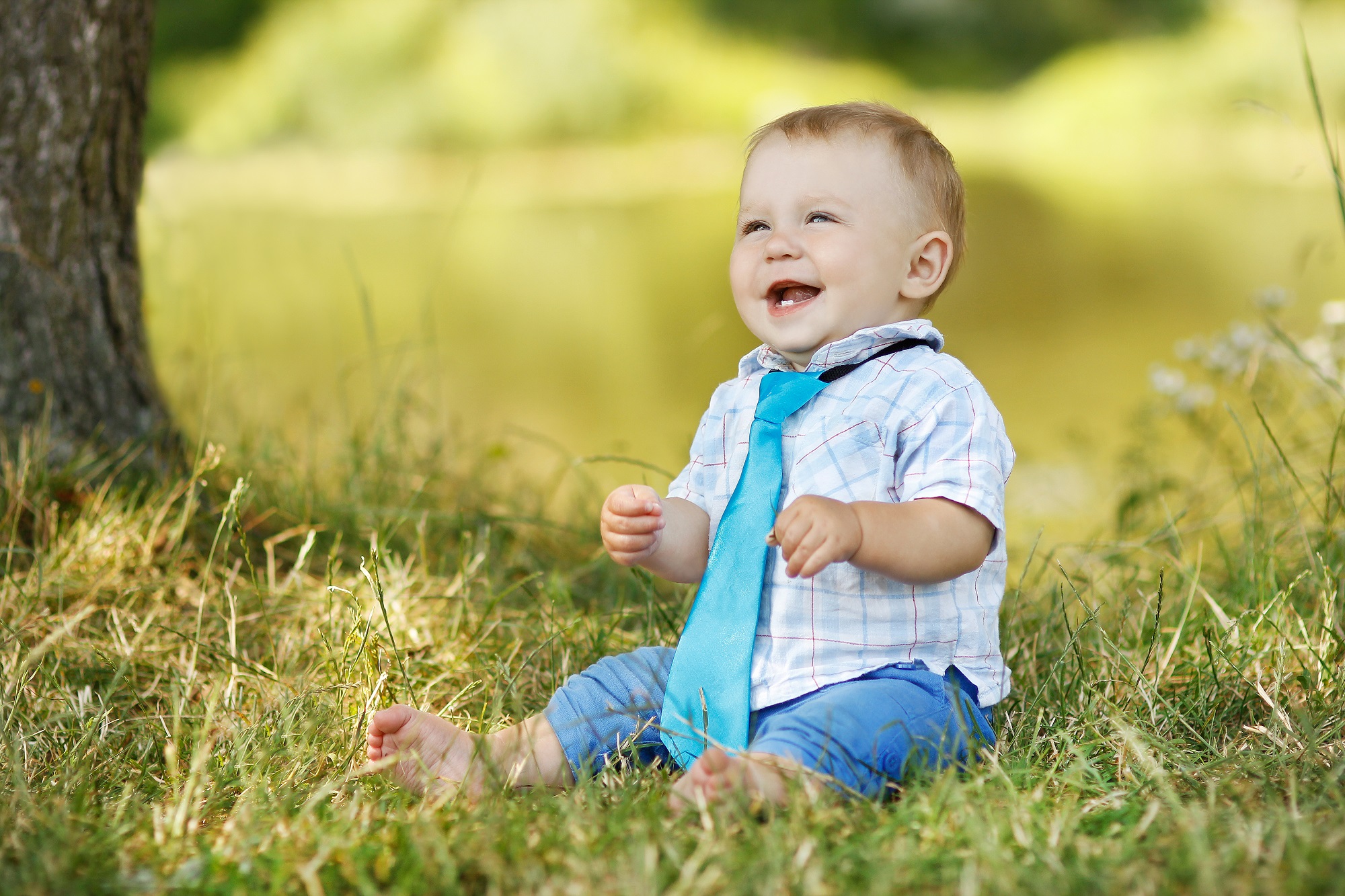 Scottish little toddler boy wearing necktie sitting on the grass and smiling brightly