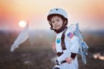 Cute little young boy in astronaut costume playing in the park during sunset