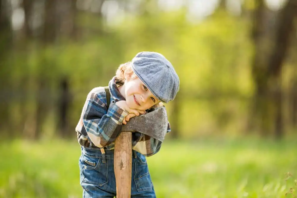 Small caucasian boy in hat posing with big axe