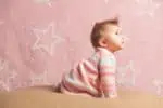 Side view of cute crawling baby girl looking up on pink background with stars on it