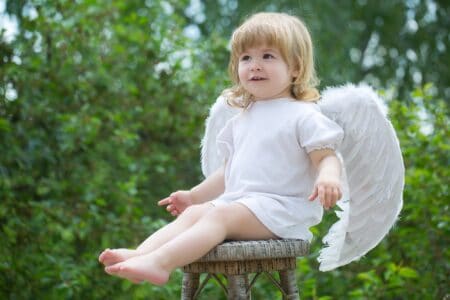 Cute little boy dressed as angel with white wings sitting on chair