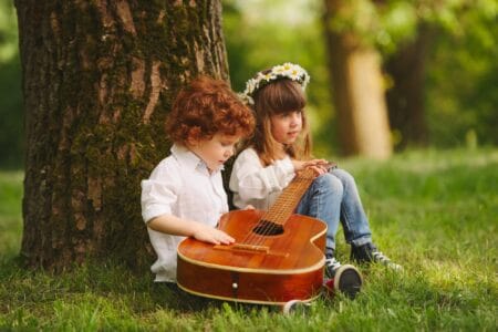 Adorable little boy and girl playing guitar in summer park