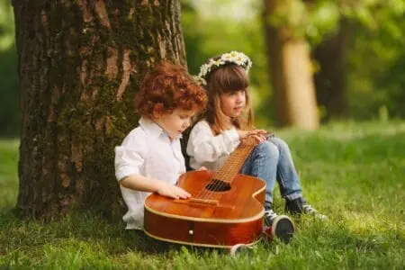 Adorable little boy and girl playing guitar in summer park