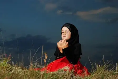 Muslim little girl on meadow before sunset
