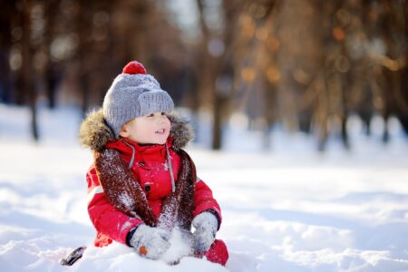 Little boy in red winter clothes having fun with snow