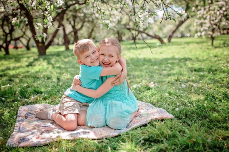 Cheerful brother and sister hugging each other tightly in the spring park