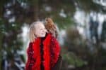 Cute girl in red scarf standing with little owl in a park