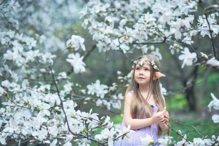 Adorable girl wearing elf costume in blooming magnolia garden