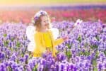 Cheerful beautiful girl with wings costume and magic wand playing in blooming flower field