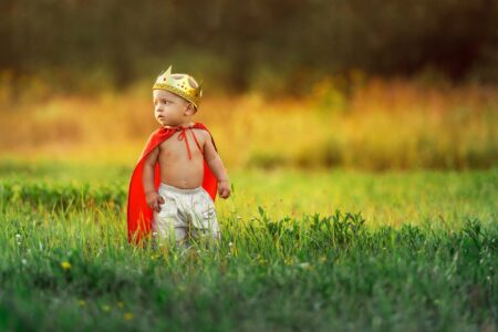 Adorable little kid wearing red cape and king crown on summer evening in the park