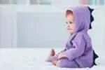 Adorable infant baby girl in dragon costume sitting on the bed