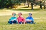 Adorable children wearing superhero costumes sitting on the grass in the park