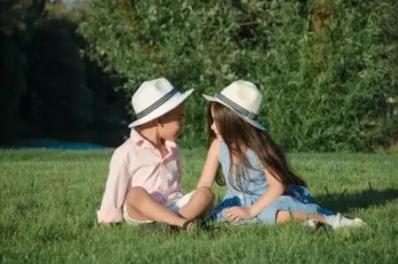 Little kids wearing hat sitting on the lawn while looking at each other