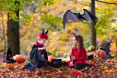 Two kids wearing devil and vampire costume with red horns and trident at the park