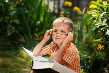 Smart kid wearing eyeglasses with book on his lap