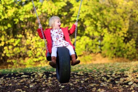 Strong adorable baby girl playing on swing at autumn park