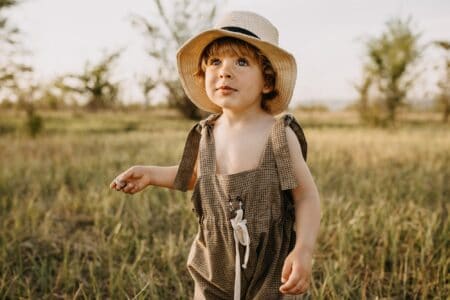 Cute little toddler boy wearing summer hat in meadow garden