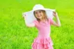 Elegant little wearing pink dress and stylish hat in bright summer day