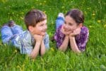 Roman kids looking at each other lying together on green grass meadow