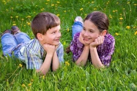 Roman kids looking at each other lying together on green grass meadow