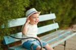 Charming little baby boy in a hat sitting on a bench in the park