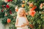 Portrait of attractive little girl against garden with roses in the background
