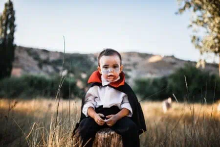 Little boy wearing vampire costume sitting in the forest