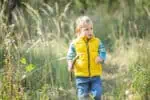 Adorable little boy with wooden stick walking on green meadow