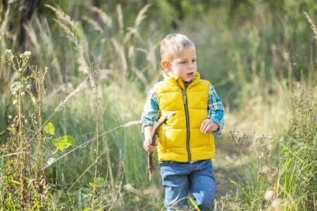 Adorable little boy with wooden stick walking on green meadow