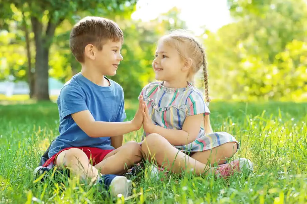 Adorable edgy little children sitting on green grass in park