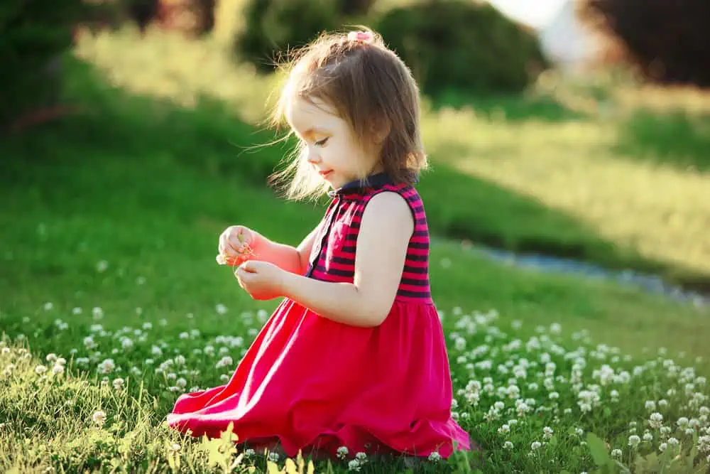 Beautiful little girl in red dress picking flowers in the park