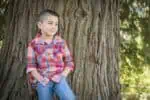 Mexican kid leaning on the tree outdoors