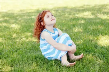 Irish little cute girl sitting on the grass looking up