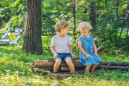 Adorable toddler boy and girl sitting on log at the forest