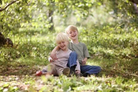 Two little boys sitting on the ground in the forest laughing happily