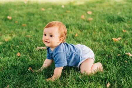 Cute little red haired baby boy crawling on fresh green grass in summer park