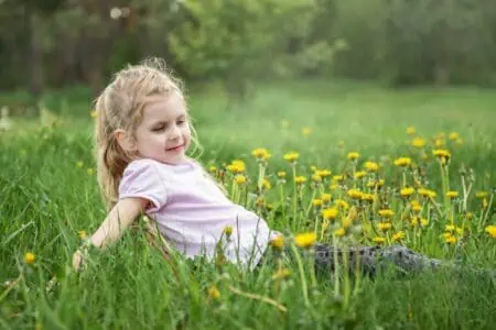 Pretty little girl lying on the flower grass in the garden