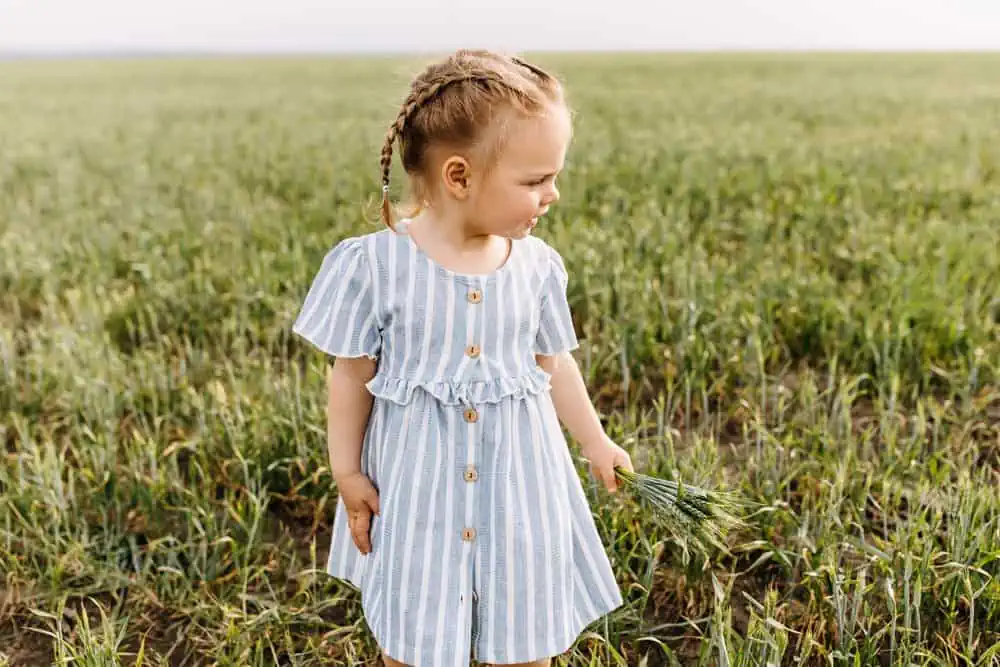 Adorable toddler girl with braided hair holding bunch of green plants in the field